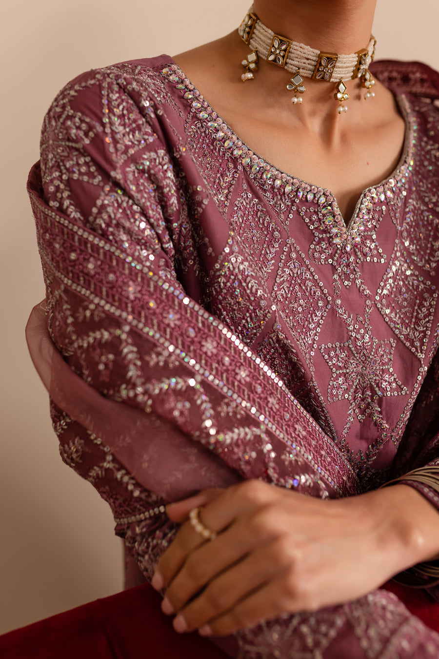 The image shows a close-up of a traditional ethnic outfit. It features intricate embroidery and sequins on a plum-colored fabric.